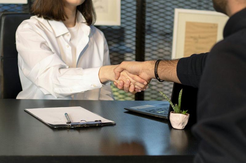 Two people shaking hands across a desk after a meeting